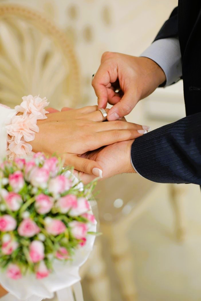 Bride holding bouquet while groom adjusts her ring
