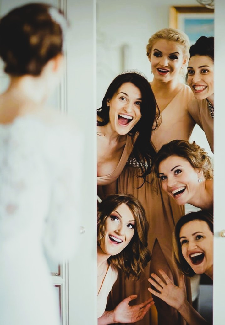 Bridesmaids helping with veil all smiling at bride
